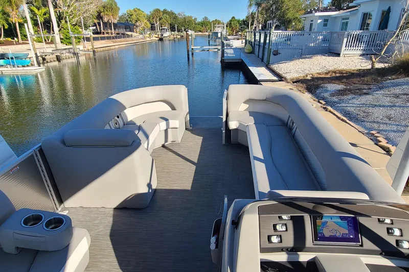 Slide: The Image of 2023 Bennington L23 pontoon boat interior with plush seating and modern dashboard on a serene canal. - 4