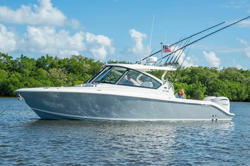 Slide: The Image of Manufacturer Provided Image: 2025 Pursuit DC 306 Dual Console boat on calm water, surrounded by lush greenery. - 2