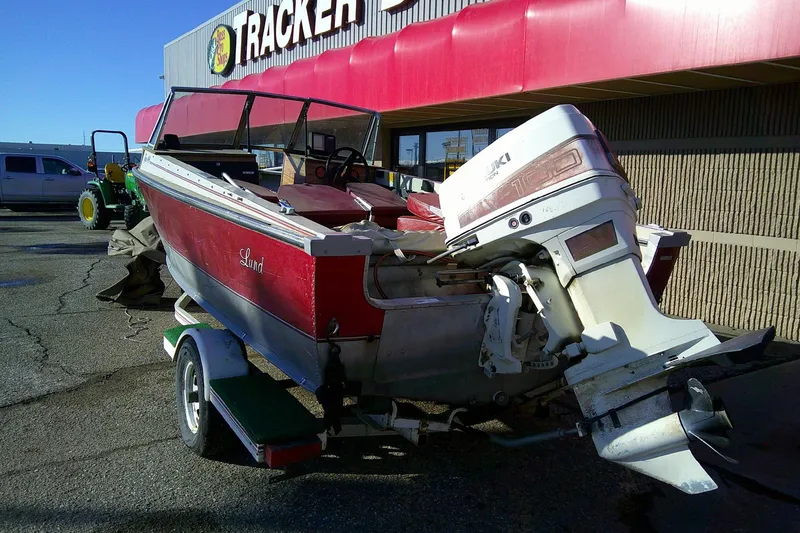 Slide: The Image of 1983 Lund 4.9 TYEE boat with Suzuki outboard motor, parked outside Tracker store. - 3