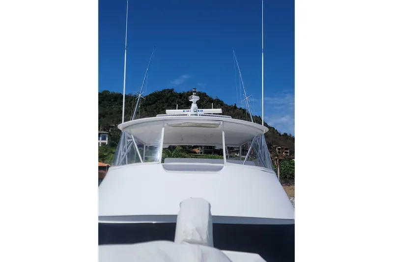 Slide: The Image of 2012 Viking 64c yacht with antennas, docked against a lush hillside under a clear blue sky. - 2