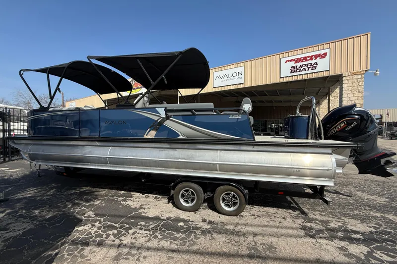 Slide: The Image of 2026 Avalon LSZ 25 Quad Lounge pontoon boat on trailer, outside dealership. - 2