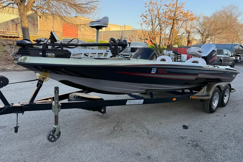 Slide: The Image of 2005 Bass Cat Puma boat on trailer, parked outdoors with trees and buildings in background. - 55