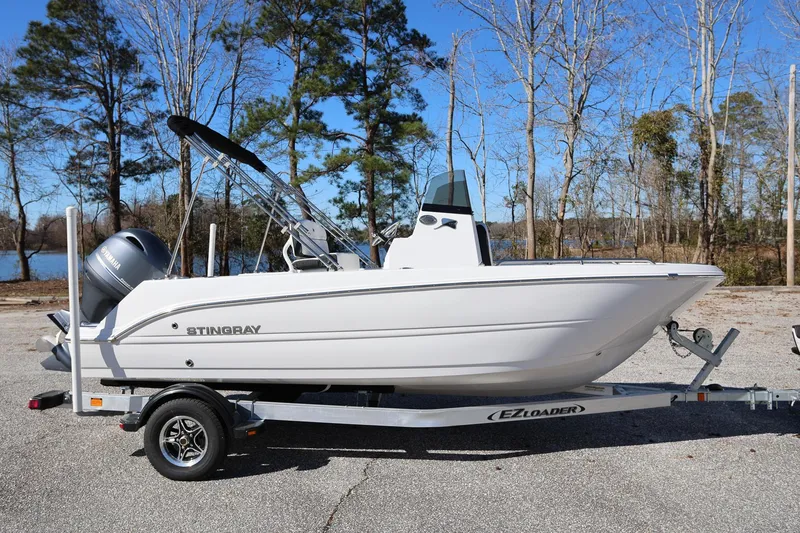 Slide: The Image of 2025 Stingray 173 CC boat on trailer, parked outdoors near trees and water. - 1
