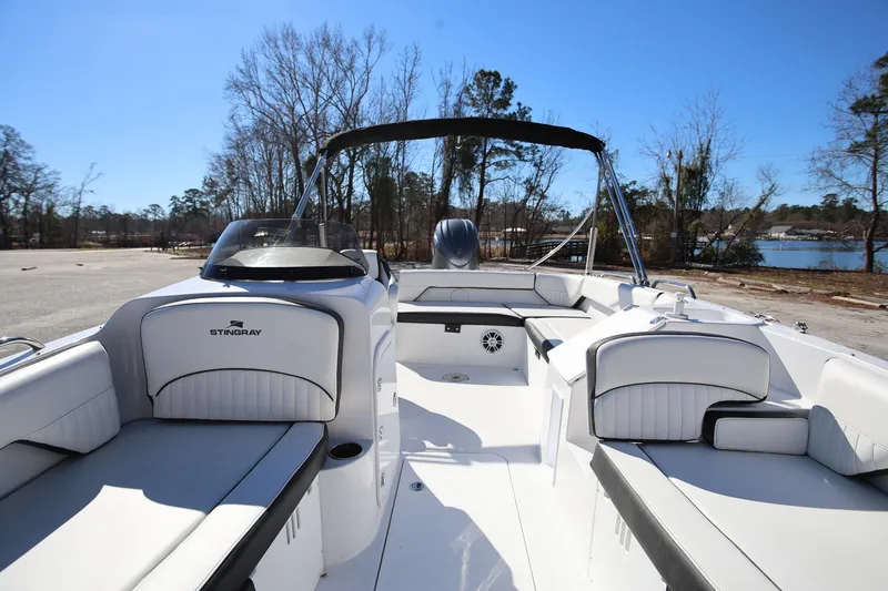 Slide: The Image of 2025 Stingray 192 SC boat interior with white seating and canopy, parked near a lake. - 27