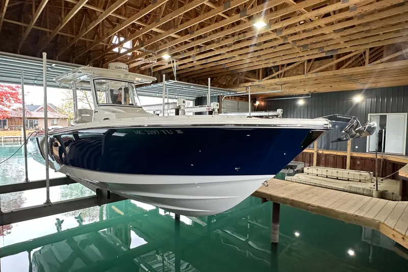 The Image of 2015 Edgewater 320CC boat docked indoors, featuring a sleek blue and white design. - 0