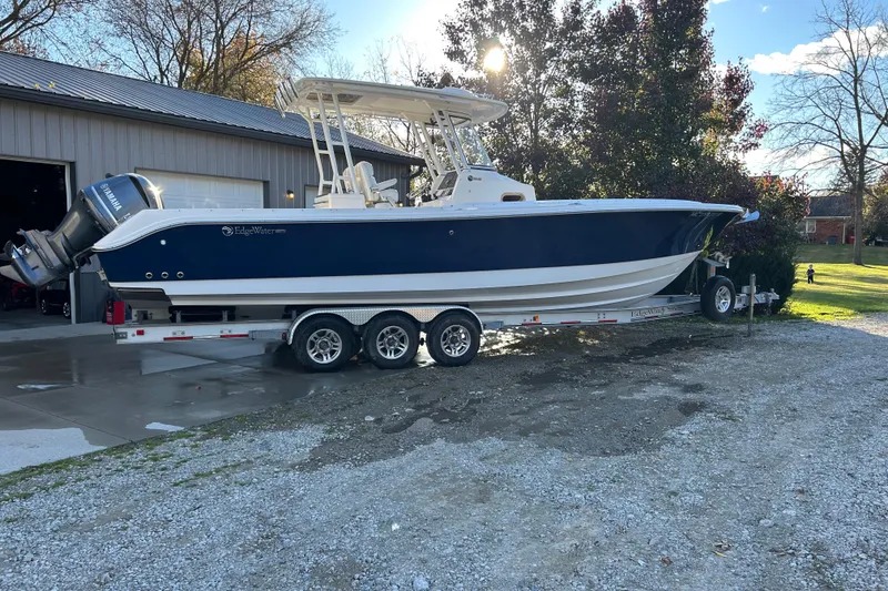 Slide: The Image of 2015 Edgewater 320CC boat on trailer, parked outside a garage on a sunny day. - 14