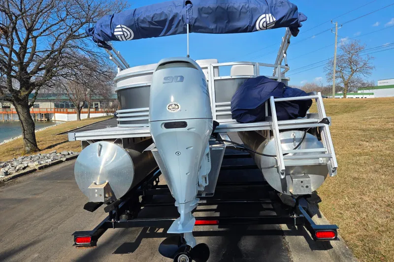 Slide: The Image of 2024 Nepallo 18TL pontoon boat with 90 HP engine on trailer, parked near a lake. - 2