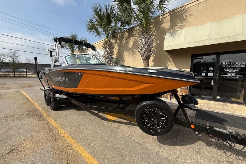 Slide: The Image of 2017 MasterCraft X46 boat on trailer, parked outside a building with palm trees. - 1