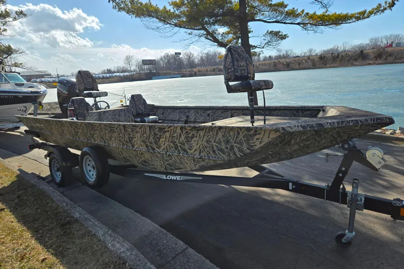 Slide: The Image of 2020 Lowe Roughneck 2070SC boat on trailer by a lake, featuring camouflage design. - 9