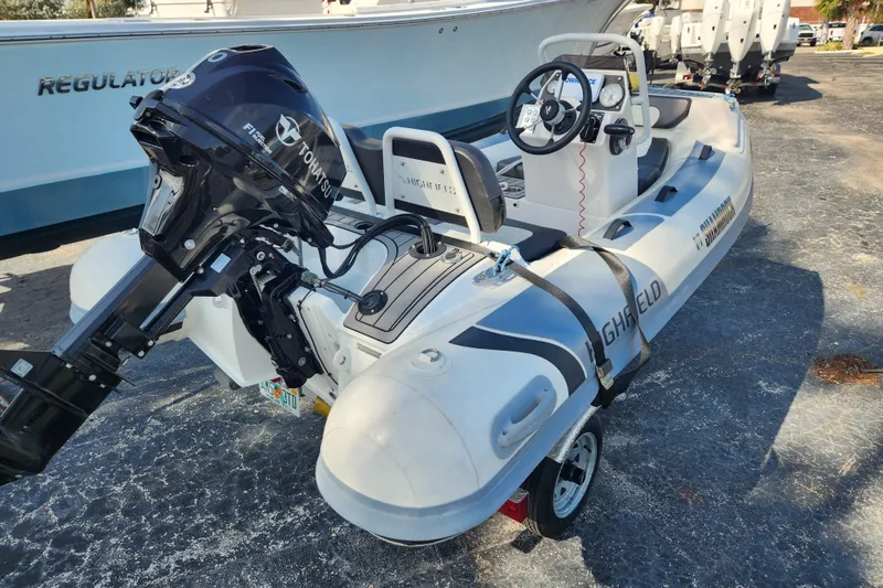 Slide: The Image of 2021 Highfield Sport 330 inflatable boat with Tohatsu outboard motor, parked on a trailer. - 2