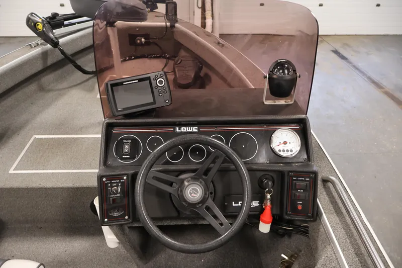 Slide: The Image of 1990 Lowe 1620V boat dashboard with steering wheel, gauges, and fish finder. - 21