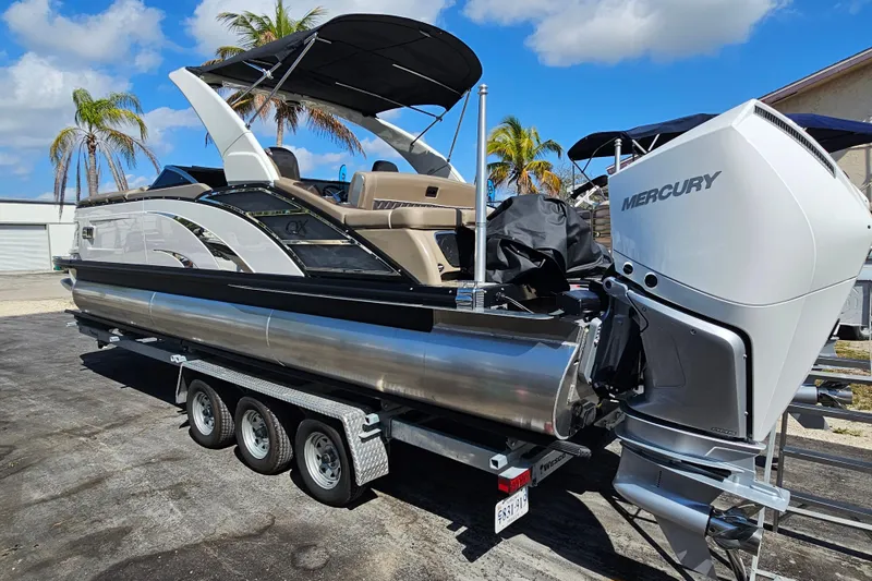 Slide: The Image of 2025 Bennington QX 27 QXSBWA X2 Swingback pontoon boat on trailer, with Mercury outboard motor. - 2