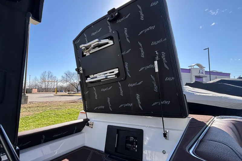 Slide: The Image of 2026 Tigé Ultré 25ZX boat interior with open storage compartment under clear blue sky. - 29