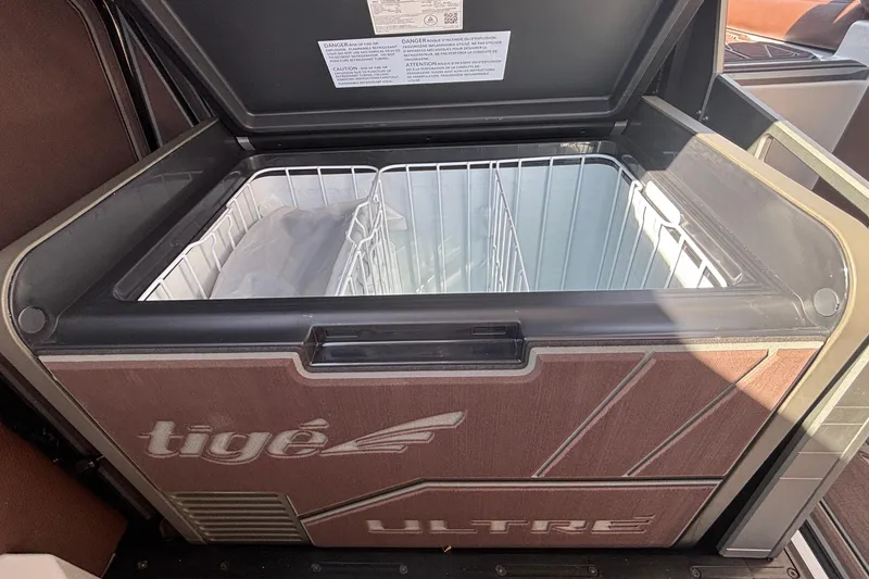 Slide: The Image of 2026 Tigé Ultré 25ZX boat cooler with open lid and wire basket. - 56