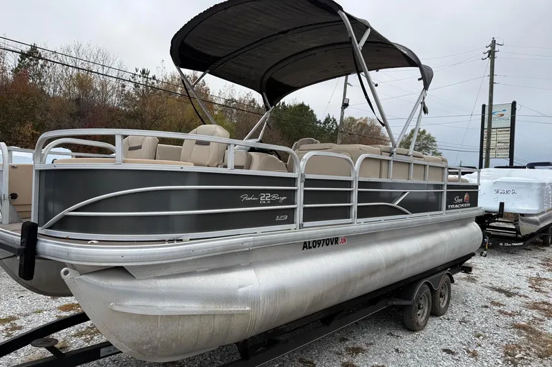 The Image of 2019 Sun Tracker Fishin' Barge 22 XP3 pontoon boat on a trailer, parked outdoors. - 0