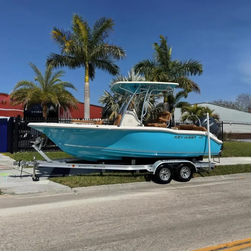 The Image of 2025 Key West 219 FS boat on trailer, vibrant blue, parked near palm trees. - 0