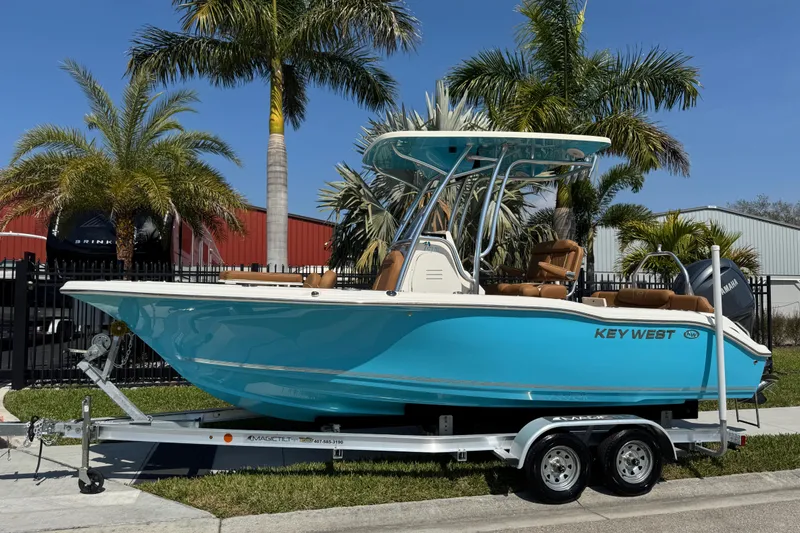 The Image of 2025 Key West 219 FS boat on trailer, vibrant blue, parked near palm trees. - 1