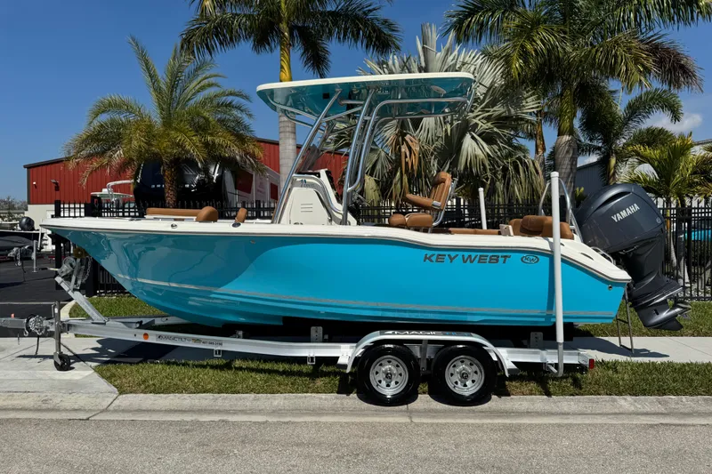Slide: The Image of 2025 Key West 219 FS boat on trailer, vibrant blue, parked near palm trees. - 2