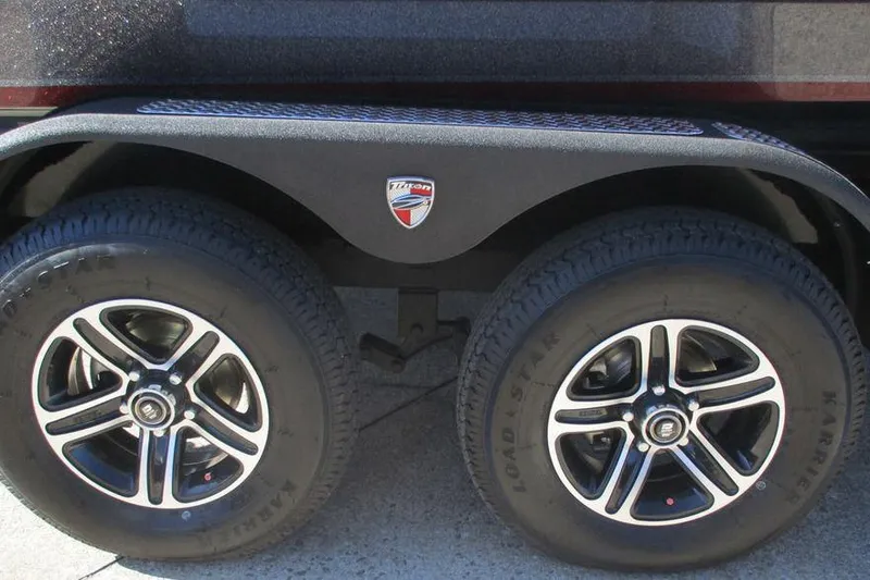Slide: The Image of 2025 Triton 19 TrX Patriot trailer wheels with black alloy rims and branded fender. - 9