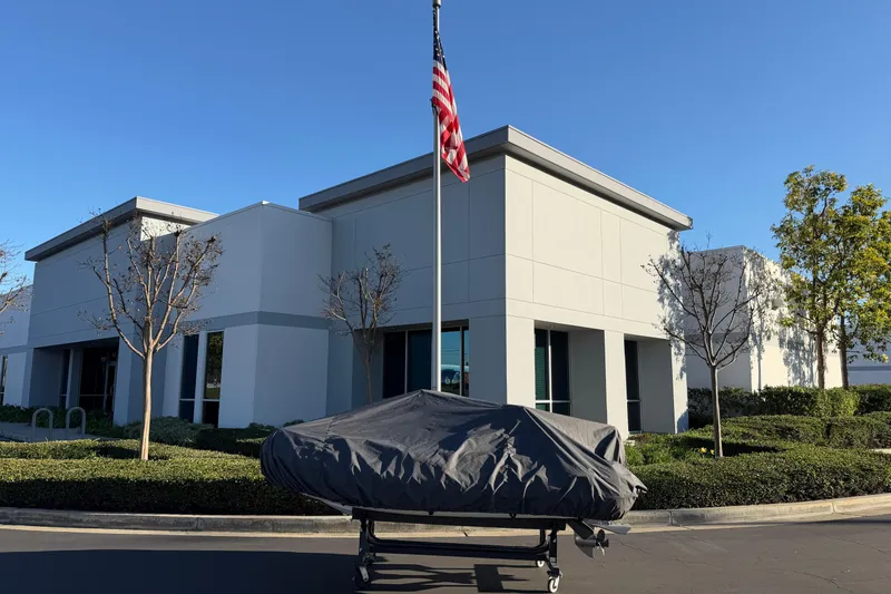 Slide: The Image of Covered Caribe C10X boat on trailer outside modern building, American flag in foreground. - 2