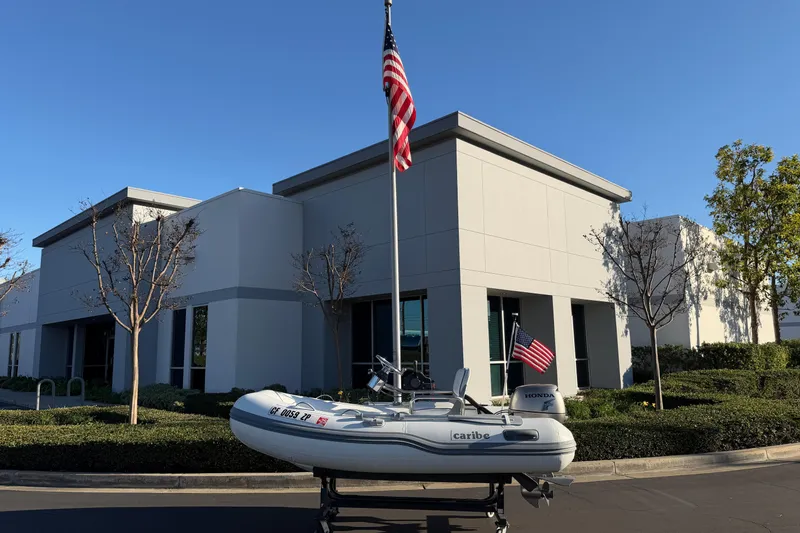 Slide: The Image of 2014 Caribe C10X inflatable boat on trailer, parked near modern building with American flags. - 3