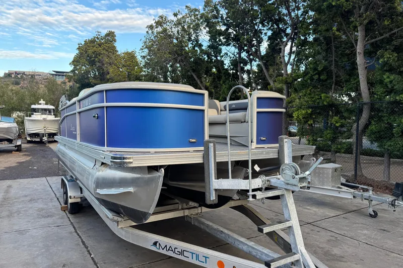 Slide: The Image of 2023 Barletta ARIA 22QC pontoon boat on trailer, surrounded by trees. - 2