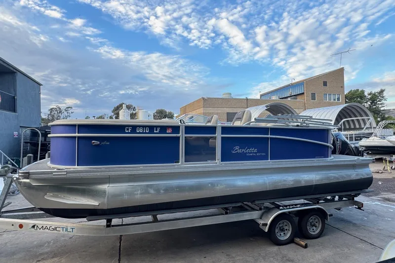 Slide: The Image of 2023 Barletta ARIA 22QC pontoon boat on trailer, parked outdoors under a cloudy sky. - 8