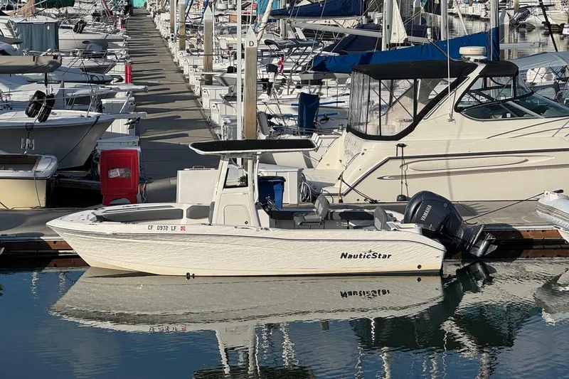 Slide: The Image of 2023 NauticStar 242L Offshore boat docked in a marina, surrounded by other vessels. - 30