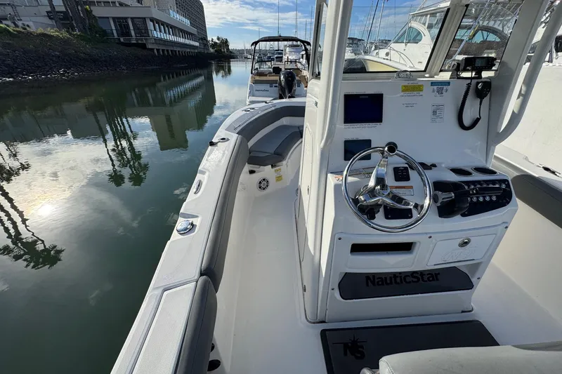 Slide: The Image of 2023 NauticStar 242L Offshore boat dashboard at marina, featuring steering wheel and controls. - 22