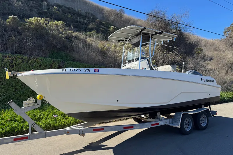 Slide: The Image of 2020 Wellcraft 222 Fisherman boat on trailer, parked roadside with scenic background. - 3
