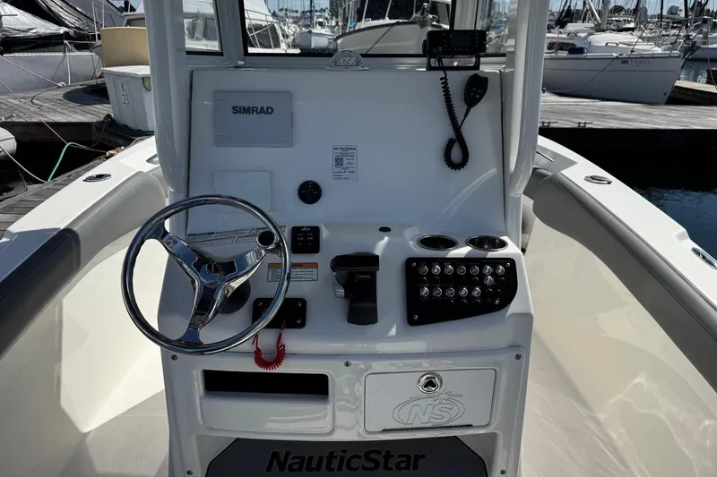 Slide: The Image of 2023 NauticStar 242L Offshore boat console with steering wheel and controls at marina. - 34