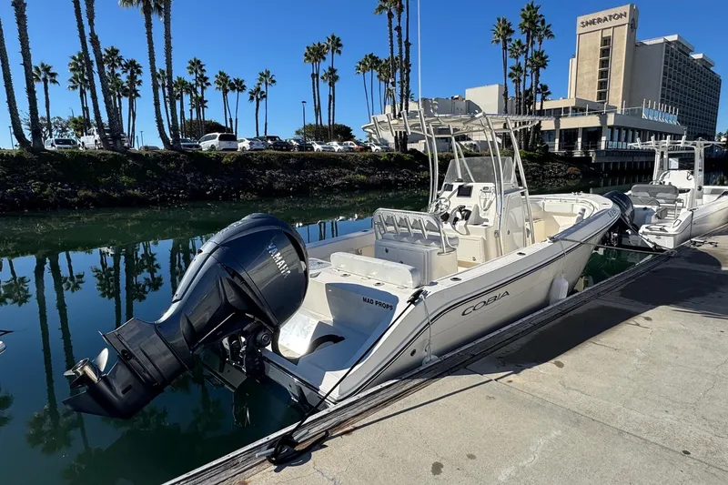 Slide: The Image of 2022 Cobia 237 Center Console boat docked near palm trees and hotel. - 2