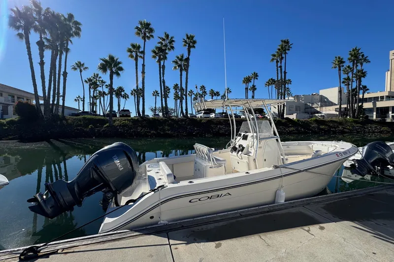 Slide: The Image of 2022 Cobia 237 Center Console boat docked by palm trees under clear blue sky. - 4