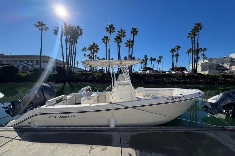 Slide: The Image of 2022 Cobia 237 Center Console boat docked under clear blue sky with palm trees. - 5