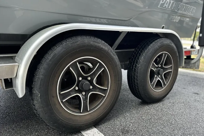Slide: The Image of 2024 Pathfinder 2200 TRS trailer wheels on asphalt, showcasing dual black alloy rims. - 13