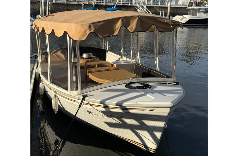 Slide: The Image of 2022 Duffy 16 electric boat with tan canopy docked on calm water. - 2