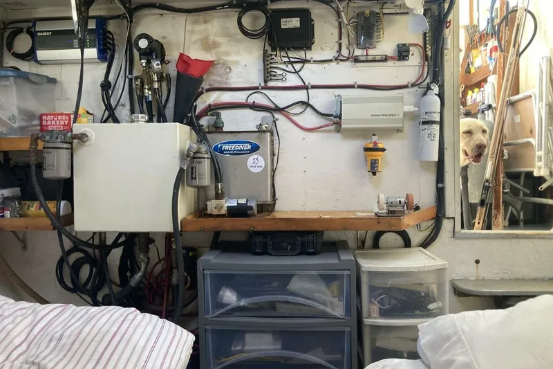 Slide: The Image of 1986 BGM Custom boat engine room with equipment, wiring, and a dog peeking through the door. - 17