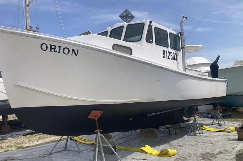 Slide: The Image of White BGM Custom 1986 boat named Orion on stands, displayed outdoors. - 35