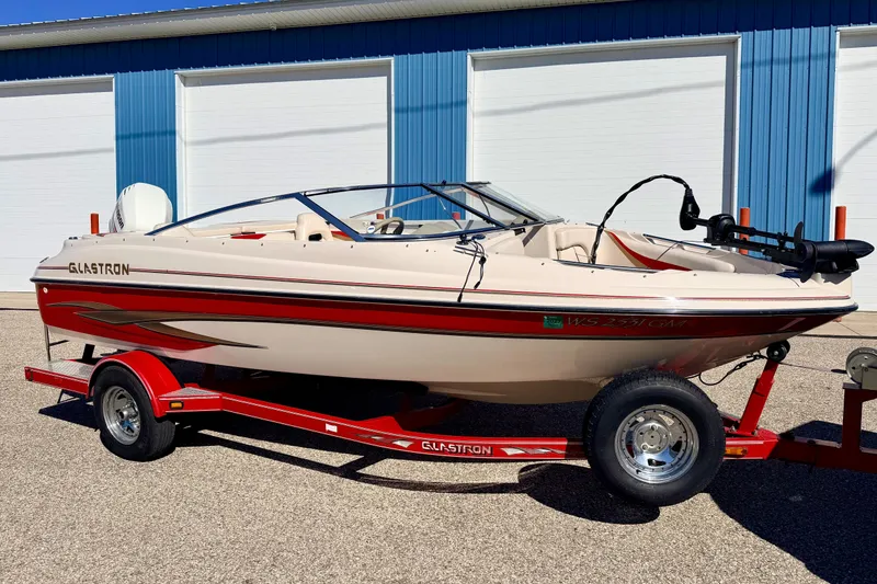The Image of 2003 Glastron/Carlson GX180 boat on red trailer, parked outside blue building. - 0