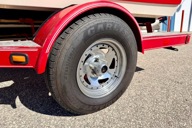 Slide: The Image of Red trailer wheel of 2003 Glastron/Carlson GX180 boat on asphalt surface. - 62