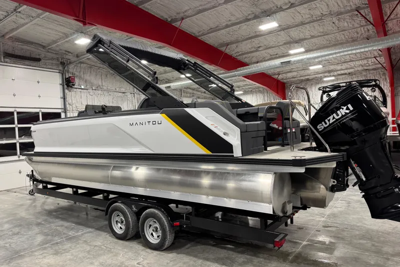 Slide: The Image of 2025 Manitou 24 Explore pontoon boat with Suzuki engine in a warehouse setting. - 5