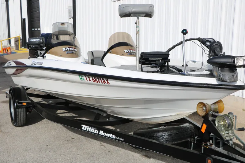 Slide: The Image of 2009 Triton 18 Explorer boat on trailer, equipped with fishing gear, parked outdoors. - 3