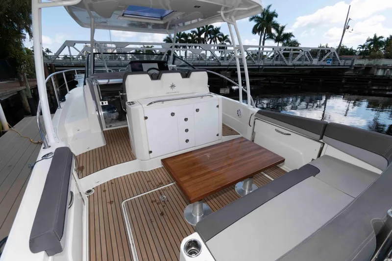 Slide: The Image of 2019 Jeanneau Leader 10.5 boat interior with seating and wooden table, docked by water. - 3