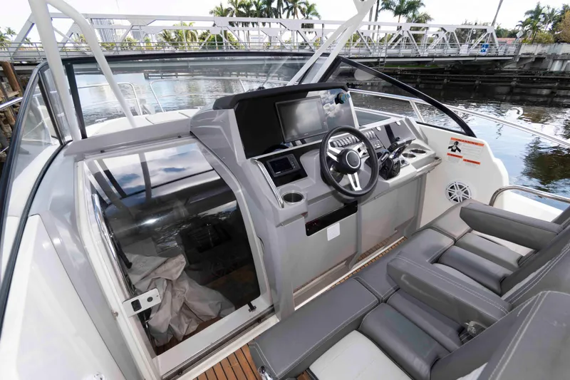 Slide: The Image of 2019 Jeanneau Leader 10.5 boat cockpit with modern steering and seating, docked near a bridge. - 8