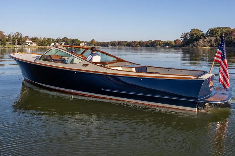 Slide: The Image of 2003 Hinckley Talaria 29 Runabout on calm water, featuring sleek design and American flag. - 1