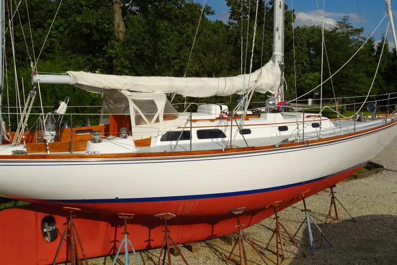 Slide: The Image of 1970 Hinckley Bermuda 40 Custom sailboat on stands, white hull, red bottom, wooded area background. - 4