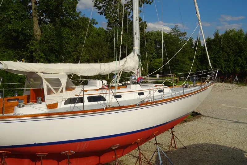 Slide: The Image of 1970 Hinckley Bermuda 40 Custom sailboat on land, white hull, red bottom, trees in background. - 5