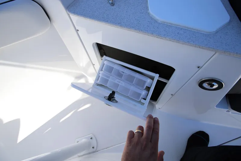 Slide: The Image of 2025 Stingray 216 CC boat storage compartment with hand accessing tackle box. - 20