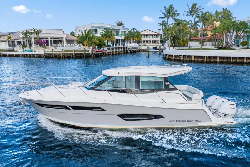 The Image of 2024 Regal 38 XO yacht cruising on a scenic waterfront with luxury homes. - 0