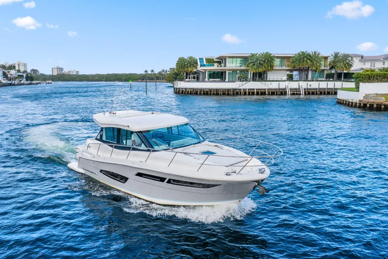 Slide: The Image of 2024 Regal 38 XO yacht cruising on a scenic waterway near luxury waterfront homes. - 6